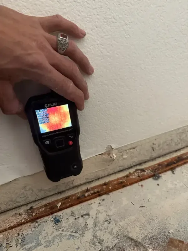 Moisture meter pressed against a wall just above the baseboard