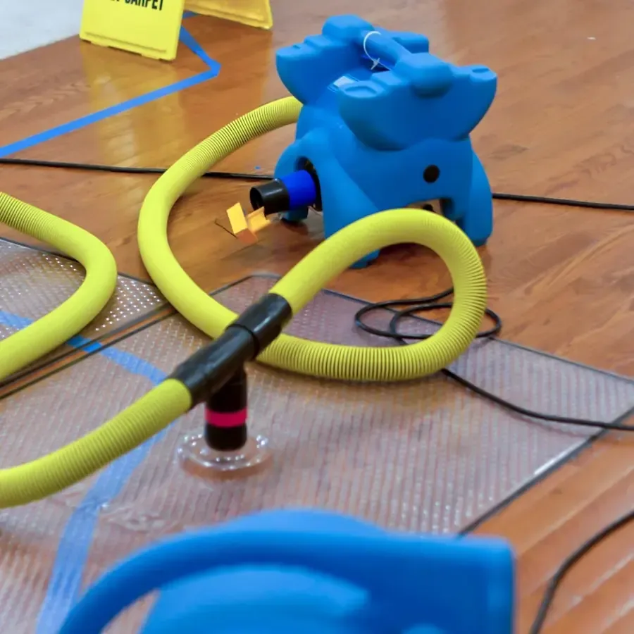 Blue air mover and yellow hose on drying mats across a wood floor
